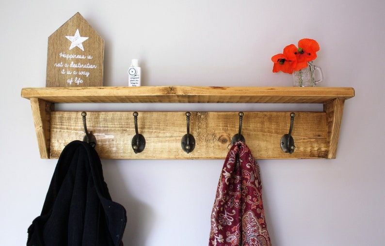 Peut inclure: Une &eacute;tag&egrave;re en bois avec cinq crochets, une petite pancarte en bois avec le texte "Le bonheur n'est pas une destination, c'est un mode de vie", et une petite bouteille de d&eacute;sinfectant pour les mains. Il y a aussi des fleurs rouges dans un bocal en verre sur l'&eacute;tag&egrave;re.