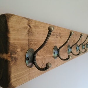 May include: A rustic wooden coat rack with eight antique brass hooks. The rack is stained a dark brown color and has a natural wood grain.