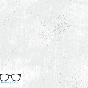 May include: White fabric with a textured, distressed appearance and subtle gray speckles. The fabric has a light, airy feel, with a brushed effect. The Nerdy Quilter logo is in the bottom left corner. Ideal for quilting and crafting projects.