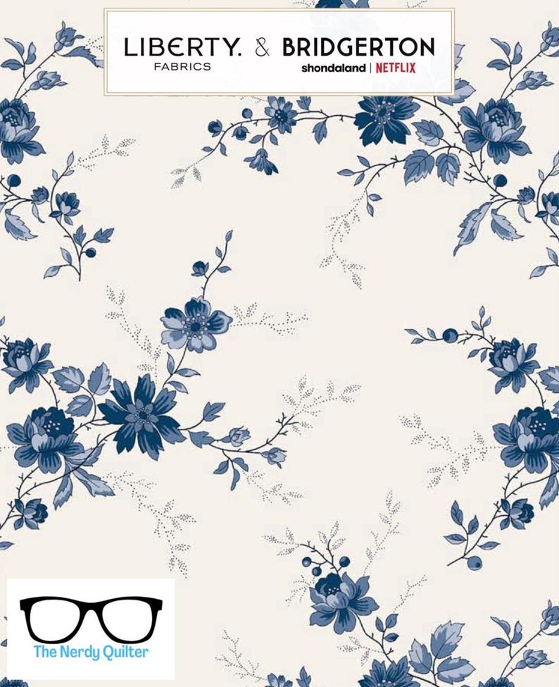 May include: A white fabric with a blue floral pattern. The fabric features a repeating pattern of blue flowers and leaves on a white background. The fabric is labeled "Liberty & Bridgerton Fabrics" and "shondaland | NETFLIX".