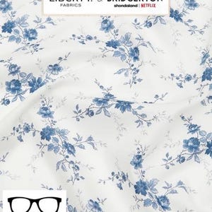 May include: White fabric with a blue floral pattern. The fabric features a repeating pattern of small blue flowers and leaves. The fabric is labeled "Liberty & Bridgerton Fabrics shondaland | NETFLIX".