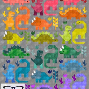 May include: A colorful quilt pattern featuring various dinosaurs in a rainbow of colors, including red, orange, yellow, green, blue, purple, and pink. The dinosaurs are arranged in a grid pattern on a gray background. The text "The Nerdy Quilter" is visible in the bottom left corner.