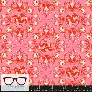 May include: A pink fabric featuring a repeating damask-style pattern with orange and red dragons enclosed in circular frames, accented by flame-like swirls. A black ruler with the text The Nerdy Quilter and Ruby Star Society is visible.