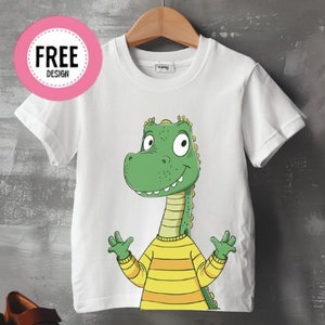 May include: White short-sleeved t-shirt with a cartoon dinosaur wearing a yellow and orange striped sweater. The dinosaur is green with a light green belly and has a big smile.