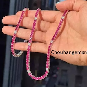 Op de afbeelding: Een delicate ketting met een reeks levendige, ronde, rode edelstenen, afgewisseld met kleine, heldere, witte stenen. De ketting wordt in een hand gehouden, wat het elegante ontwerp en het kleurcontrast benadrukt. De sieraden staan tegen een vage achtergrond.