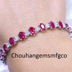 May include: A silver bracelet with oval, deep red gemstones and smaller, clear stones. The bracelet is shown on a wrist, highlighting the design. The text "Chouhanggemsmfgco" is visible. The gemstones are likely set in a silver metal.