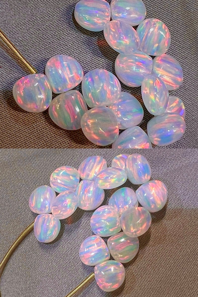 May include: A collection of iridescent opal gemstones. The opals are oval-shaped, displaying a play of color with hues of pink, blue, and green. They are arranged on a textured gray surface, with a gold chain visible.