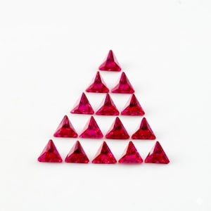 Puede incluir: Una disposición piramidal de gemas triangulares, facetadas, de color rojo rubí sobre un fondo blanco. Las gemas, espaciadas uniformemente, reflejan la luz, resaltando sus bordes afilados y su color vibrante. Ideal para la fabricación de joyas o manualidades. Cada gema mide aproximadamente 0,5 cm.