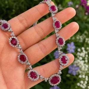 May include: A necklace featuring oval-cut ruby gemstones surrounded by small, sparkling diamonds. The rubies are a deep red color, and the diamonds are clear. The necklace is set in a silver or white gold setting.