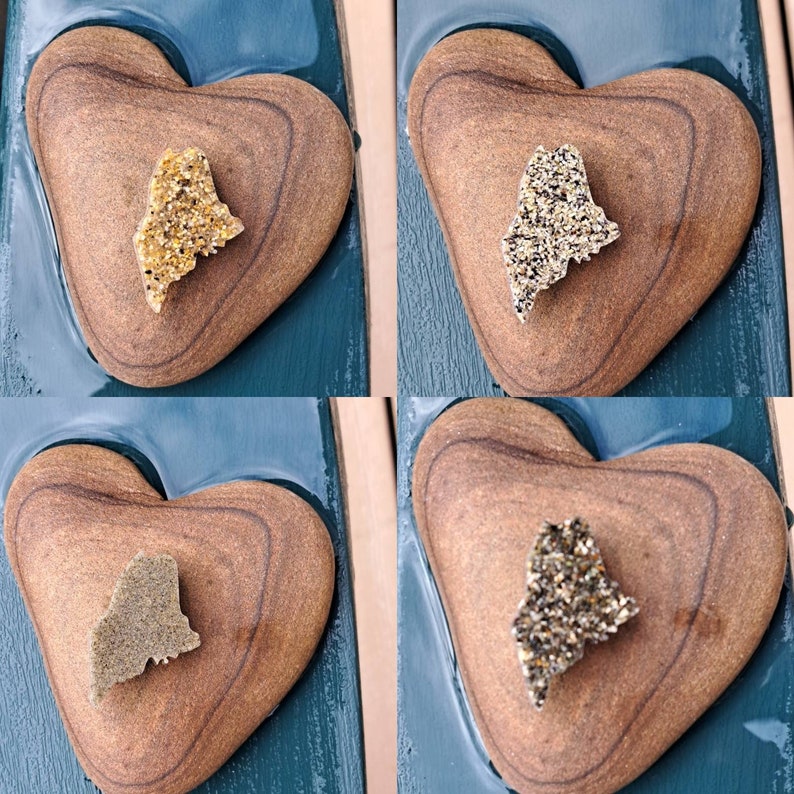 May include: Four wooden heart-shaped ornaments with a gold glitter outline. Each heart features a cutout of the state of Maine, filled with different colored glitter.