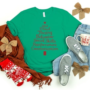 Op de afbeelding: Een groen T-shirt met een rood kerstboomontwerp. De boom is gemaakt van de woorden "ABA", "Mand", "Tacting", "Behavior", "Social Skills", "Reinforcement" en "Communication".