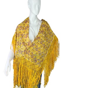 Puede incluir: Un chal amarillo con un patrón geométrico y flecos. El chal está hecho de una tela suave y ligera, perfecto para agregar un toque de color a cualquier atuendo.