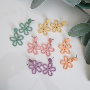May include: A collection of colorful flower-shaped earrings in various pastel shades, including green, yellow, pink, orange, and purple. Each pair features a stud and a dangling floral design, perfect for adding a touch of whimsy to any outfit.