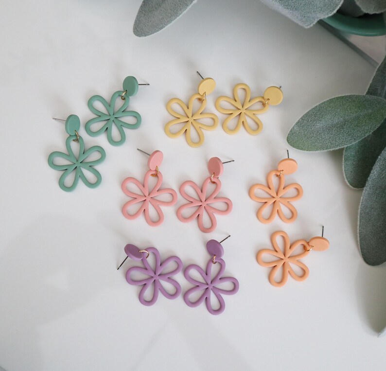 May include: A collection of colorful flower-shaped earrings in various pastel shades, including green, yellow, pink, orange, and purple. Each pair features a stud and a dangling floral design, perfect for adding a touch of whimsy to any outfit.