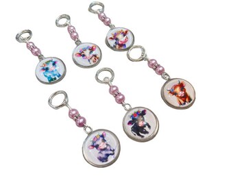 May include: A collection of six cow-themed keychains. Each keychain features a round, silver-toned charm with a colorful cow illustration. The charms are connected to a string of pink beads and a silver-toned ring. The cows have floral crowns.