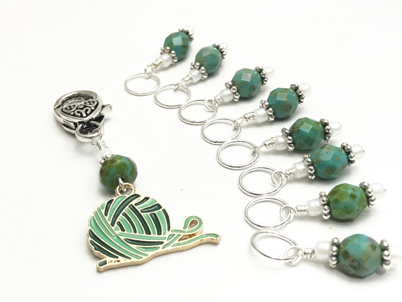 May include: Set of 7 turquoise and silver stitch markers with a yarn ball charm. Each marker features a turquoise bead with silver accents and a silver ring.