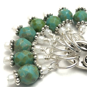 May include: A set of 7 stitch markers with a heart-shaped charm. The markers are silver with turquoise and white beads.