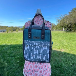 May include: A teal and gray backpack with a llama print. The backpack has a zipper closure and two adjustable straps.