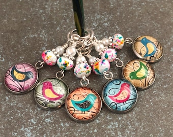 May include: Set of six colorful bird stitch markers with white and multi-colored beads. The markers are round and feature a variety of bird designs.