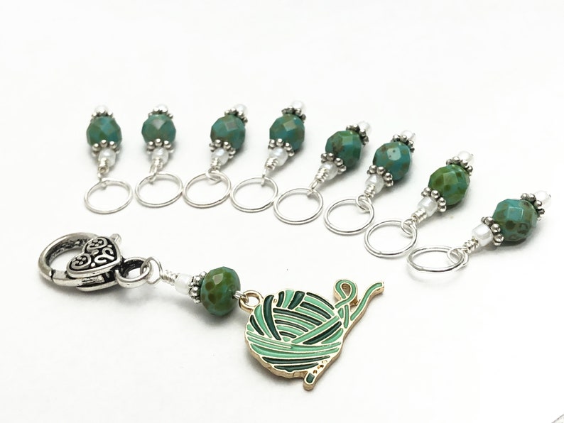 May include: Set of eight teal green and silver stitch markers with a silver heart-shaped clasp and a charm of a green yarn ball.