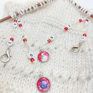 May include: Three sets of stitch markers with snowman charms. Each set has a silver chain with red and clear beads and a white number bead. The numbers are 2, 4, 9, 0, 1, 5, 7, 8, and 9.