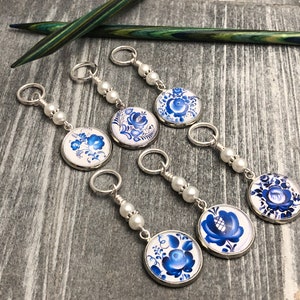 Puede incluir: Seis marcadores de punto azul y blanco con flores con cuentas de perlas. Los marcadores de punto están unidos a anillos plateados.