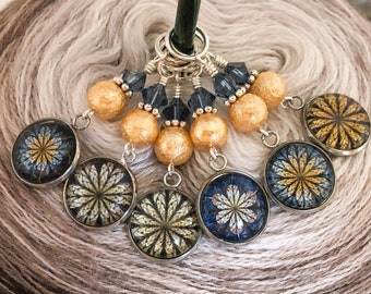 May include: Six gold and blue glass stitch markers with a floral design. The markers are attached to a silver ring with a silver bead and crystal accents.
