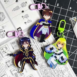 May include: Three acrylic keychains featuring anime-style characters. One character has brown hair and a blue cape, one has dark blue hair and a black and gold outfit, and one has long yellow hair and a white and black suit with a lime green clasp.
