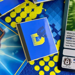 Peut inclure: Une épingle en émail bleue et jaune représentant une lettre D stylisée avec un design pixelisé. L'épingle est sur un fond jaune et bleu.