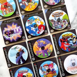 May include: A collection of colorful video game coasters featuring various characters and game titles. The coasters are round and come in black packaging. Games include "Animal Town", "Speed Heroes", and "Harvest Season".