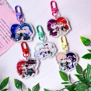May include: Six colorful keychains with clear acrylic charms featuring anime-style couples. Each charm has a different couple with unique designs and poses. The keychains are attached to metal rings with colorful clasps.