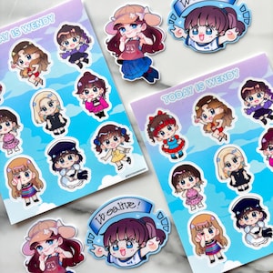 Puede incluir: Una colección de pegatinas coloridas con ilustraciones de dibujos animados de una niña con varios atuendos y peinados. Las pegatinas están sobre un fondo azul claro con el texto "TODAY IS WENDY" y "We alive!".