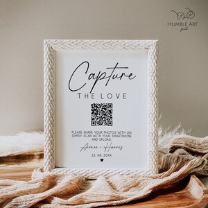 May include: White framed sign with the text "Capture the Love" and a QR code. The text below the QR code reads "Please share your photos with us! Simply scan with your smartphone and upload. Aimee & Harris 12.08.20XX".