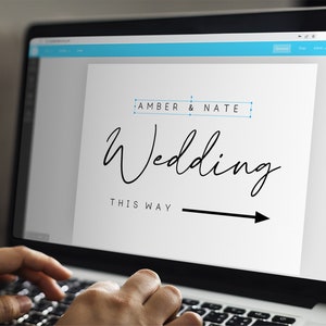 May include: A computer screen displaying a wedding sign with the text "Amber & Nate Wedding This Way" and an arrow pointing to the right.