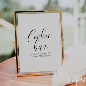 May include: A gold-framed sign with the text "Cookie Bar" in a cursive font. The sign also includes the text "A sweet ending to a new beginning".