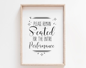 May include: A white sign with black text in a light wood frame. The sign reads "Please remain seated for the entire performance".