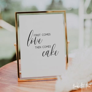 May include: A gold-framed sign with the text "First comes love then comes cake" in black calligraphy font.