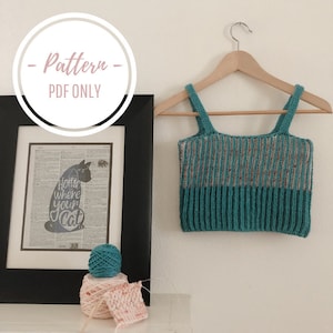 May include: A knitting pattern for a teal and pink striped tank top. The pattern is available as a PDF download only. The image shows a completed tank top on a hanger, yarn balls, and a framed print with the text "Hottie where your cat"