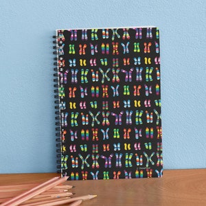 May include: A black spiral notebook with a colorful chromosome pattern. The chromosomes are arranged in a repeating pattern and are colored in a rainbow pattern.