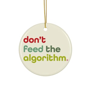 Puede incluir: Adorno redondo de cerámica blanquecina con el texto "don't feed the algorithm." en rojo, verde y amarillo verdoso. El adorno cuelga de una cuerda dorada.
