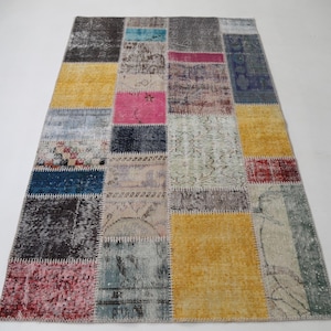 May include: A rectangular patchwork rug with a variety of colors and patterns. The rug features squares of yellow, pink, blue, and gray, with visible stitching. The rug is a vintage style and would be suitable for a living room or bedroom.