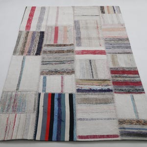 Könnte beinhalten: Rechteckiger Patchwork-Teppich mit neutralem Hintergrund und farbenfrohen Streifen und Mustern. Der Teppich hat eine Vielzahl rechteckiger Patches in Weiß-, Rot-, Blau- und Grautönen. Der Teppich besteht aus gewebtem Stoff.