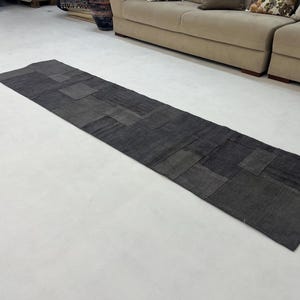 以下が含まれることがあります： パッチワーク生地で作られた、長方形のグレーのランナーラグ。ラグはさまざまなグレーの生地で作られており、微妙な質感があります。