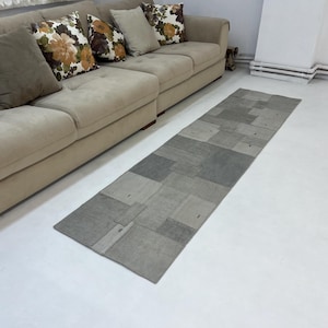 May include: A grey and white patchwork runner rug with a rectangular shape. The rug is made of different pieces of fabric sewn together.