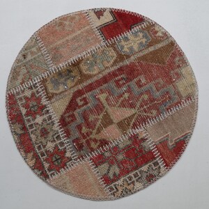 Könnte beinhalten: Runder Patchwork-Teppich im Vintage-Stil. Der Teppich zeigt eine Mischung aus gedämpften Farben, darunter Rot, Beige und Braun, in einem geometrischen Muster. Die Flicken sind mit weißen Nähten verbunden, was ihm ein einzigartiges, handgefertigtes Aussehen verleiht.