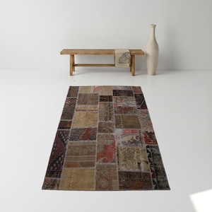 May include: A rectangular patchwork rug with a variety of colors and patterns. The rug features a mix of brown, beige, and burgundy patches, creating a vintage aesthetic. The rug is placed on a white floor.