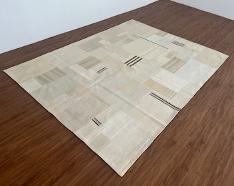 May include: A white patchwork rug with brown stripes. The rug is made of different pieces of fabric sewn together.