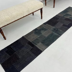 Puede incluir: Una alfombra larga y rectangular de patchwork hecha de diferentes tonos de gris y azul. La alfombra está hecha de materiales reciclados y tiene un aspecto rústico y vintage.