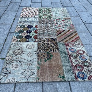 Könnte beinhalten: Ein Patchwork-Teppich mit verschiedenen floralen und geometrischen Mustern in Braun-, Beige-, Blau-, Grün- und Rottönen. Der Teppich ist aus recycelten Materialien hergestellt und hat einen Vintage-Look.