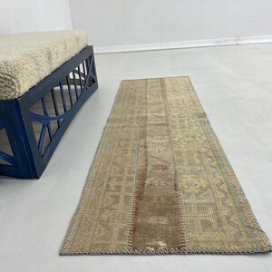 以下が含まれることがあります： ベージュ、ブラウン、色あせた赤色のパッチワークデザインの長方形のヴィンテージスタイルのラグ。 ラグは明るい色の床に置かれ、背景にはクリーム色のクッションが付いた青いベンチがあります。